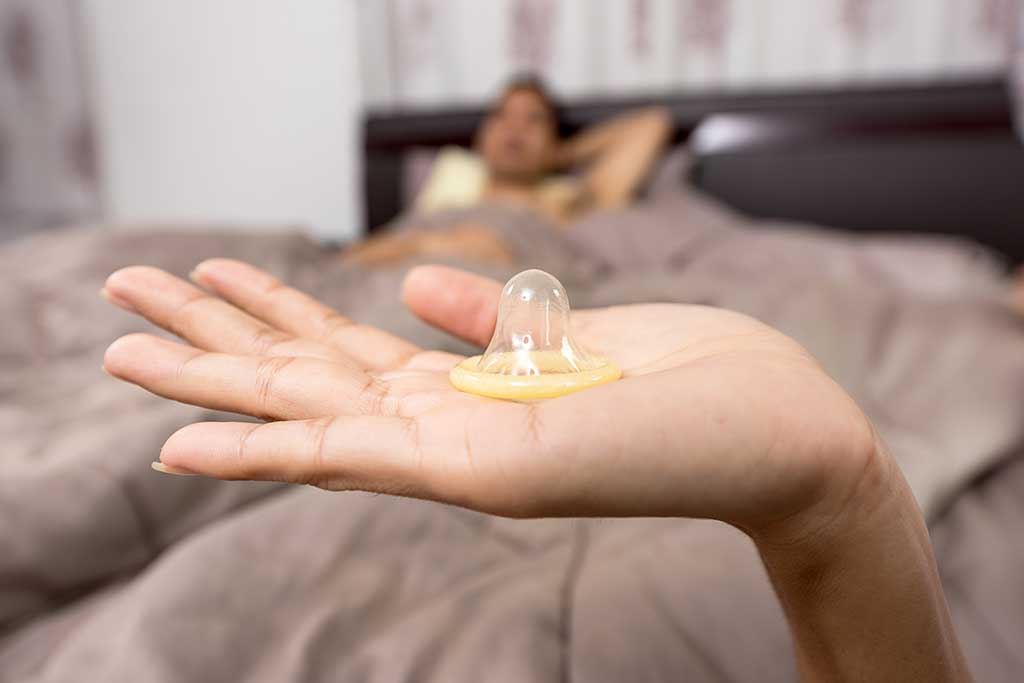 woman holding condom with man in bed